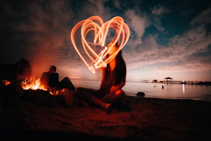 Woman creating a heart shape with sparklers on a beach