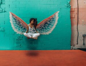 A woman sitting cross legged in front of a mural of Angel wings, making her look like she is levitating 